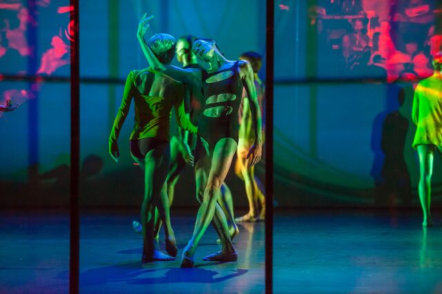 A dancer in a cut-out leotard cradles another's head in the crook of her arm